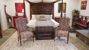 Ein Bett mit Himmel, ein Teppich mit Blumenmuster, zwei Sessel, eine Holzbank und ein rotes Sofa.
