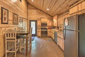 Una cocina de estilo cabaña de madera con una mesa de comedor, sillas, un refrigerador, un microondas, un horno y armarios de madera.