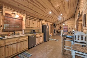 L’intérieur d’une cabane en bois comprend une cuisine équipée de meubles en bois, d’un réfrigérateur et d’un coin repas avec une table et des chaises.