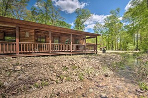Une cabane rustique dotée d’une terrasse en bois et d’un petit étang en premier plan.