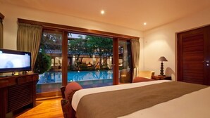 A hotel room with a large bed, a television, a dining table, and a view of an outdoor swimming pool.