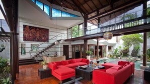 A spacious living area with a red sectional sofa, a staircase, and a view of the outdoor garden.
