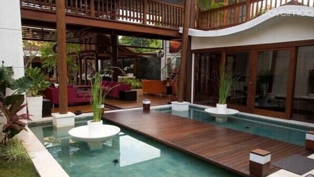 A modern outdoor pool area with wooden decking, seating, and potted plants.
