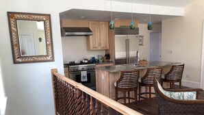 A modern kitchen with a central island, wooden bar stools, and a decorative mirror. - Beautiful Carriage House on the Chop (Oak Bluffs)