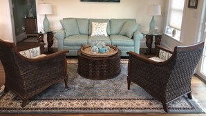 A living room with a green sofa, two armchairs, a coffee table with decorative items, a patterned rug, and a painting of a seascape. - Beautiful Carriage House on the Chop (Oak Bluffs)