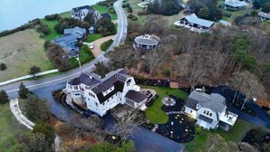An aerial view of a residential area with multiple houses, a winding road, and a large lawn. - Beautiful Carriage House on the Chop (Oak Bluffs)