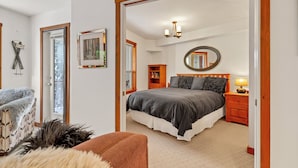 Une chambre à coucher avec un grand lit, une table de chevet en bois, un miroir et une porte donnant sur une autre pièce.
