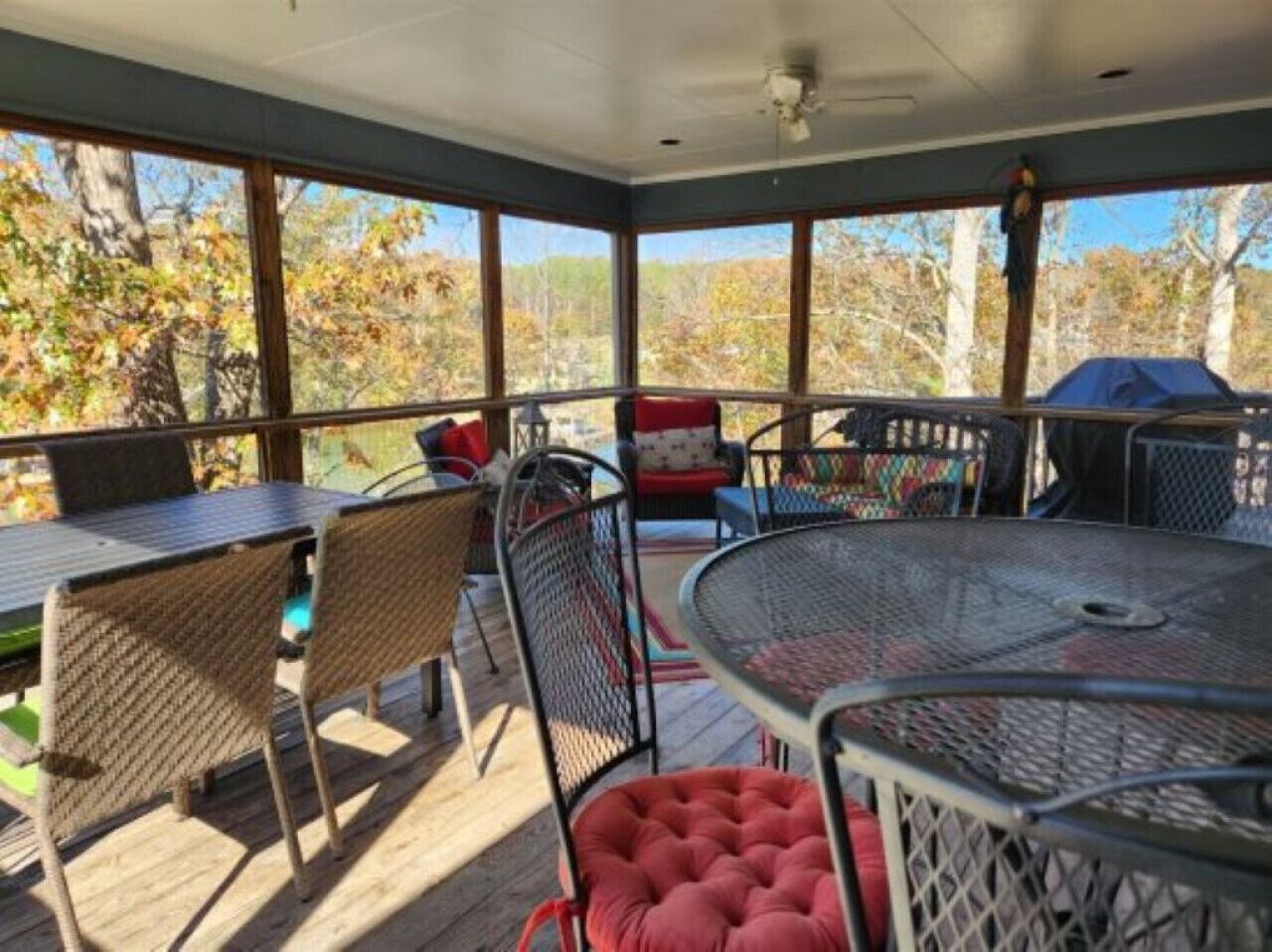 A covered outdoor seating area with metal tables and wicker chairs, overlooking a forested area.