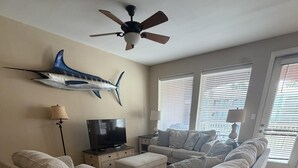 A living room with a large sectional sofa, a flat-screen TV, and a ceiling fan. - Vitamin Sea- 40 HT (Laguna Vista)