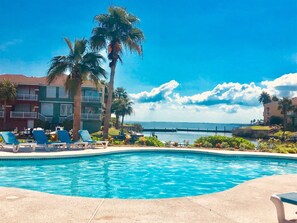 A swimming pool with lounge chairs, palm trees, and a view of the ocean.
