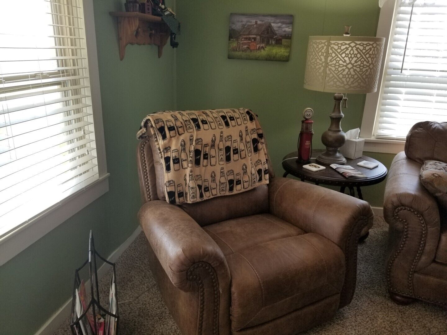 Un sillón de cuero marrón con una manta, una lámpara y un cuadro en la pared.