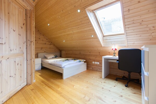 Un dormitorio con techo inclinado, paredes de madera, cama, escritorio y silla.