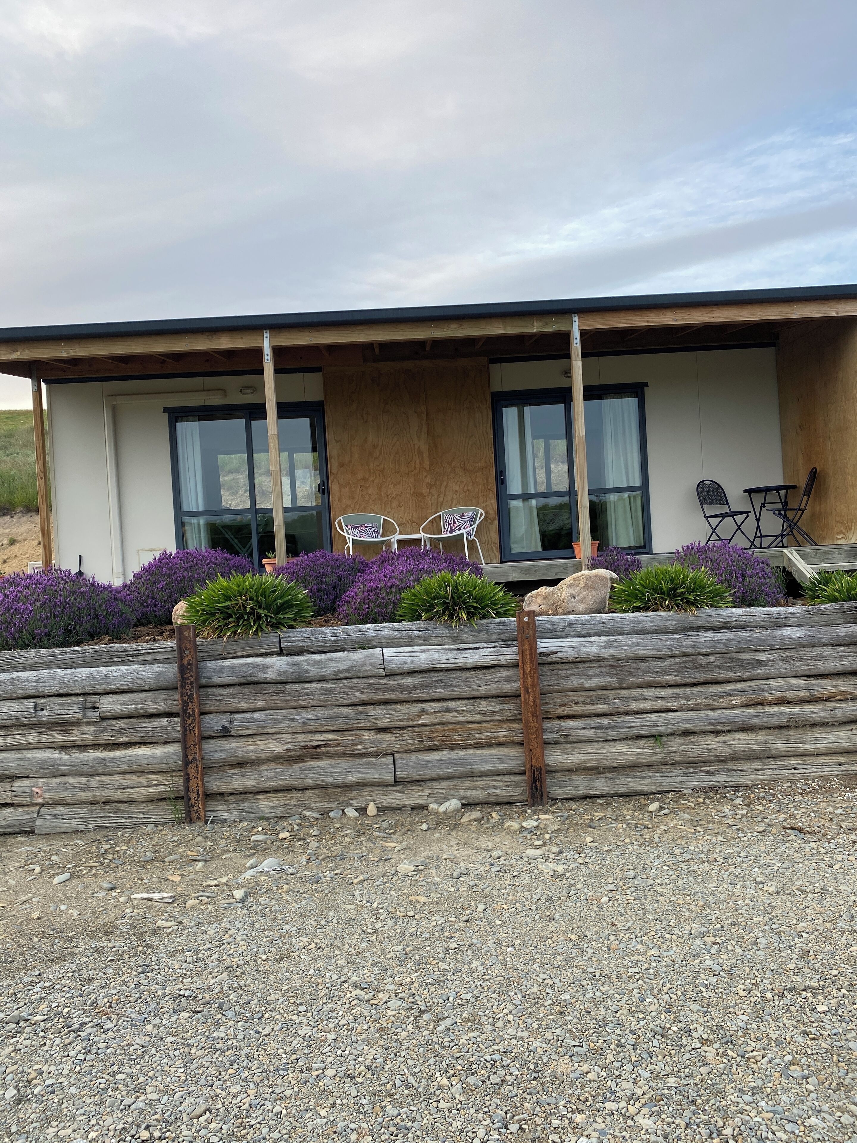 Un bâtiment moderne doté de grandes fenêtres, d’une terrasse en bois et d’un espace salon extérieur.