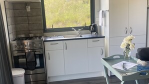 Eine kompakte Küche mit Gasherd, Backofen und Spüle, ein Fenster mit Blick auf Grünflächen und ein kleiner Tisch mit einem Blumenstrauß.