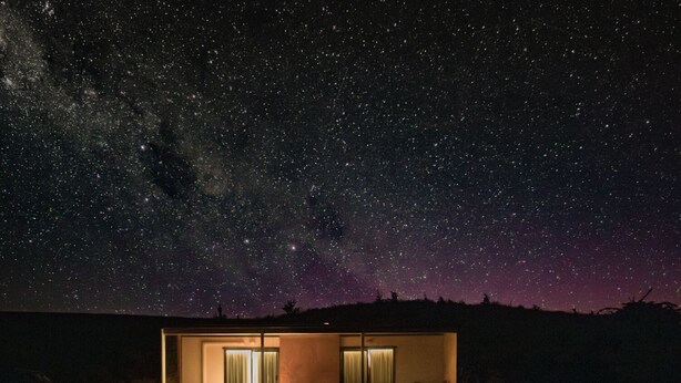 Ein modernes Haus mit großem Fenster und einer Tür, unter einem sternenübersäten Nachthimmel.