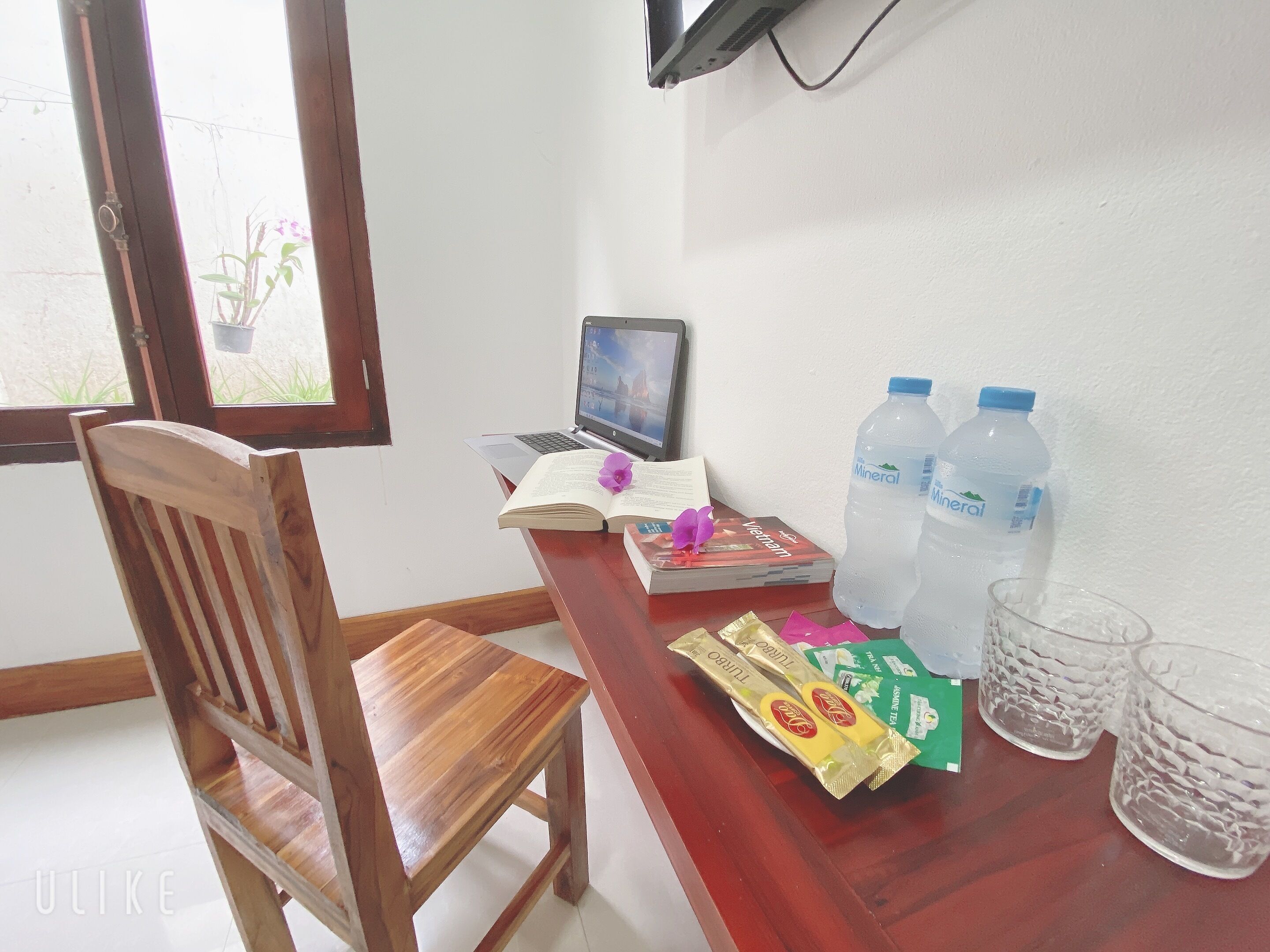 Una silla de madera, un escritorio con una computadora portátil, libros, botellas de agua y paquetes de comida.
