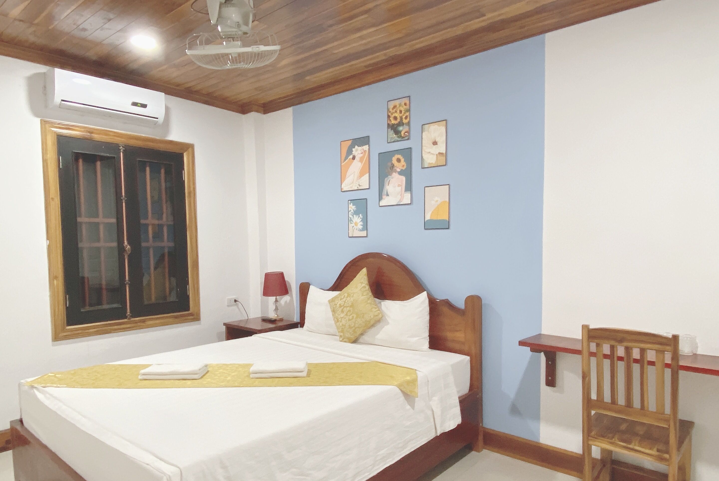 Una cama bien tendida con un cabecero de madera, una mesita de noche con una lámpara y una ventana con marco de madera.