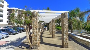 Ein gepflasterter Weg mit Steinpfeilern, einer weißen Pergola und einer Reihe geparkter Autos.