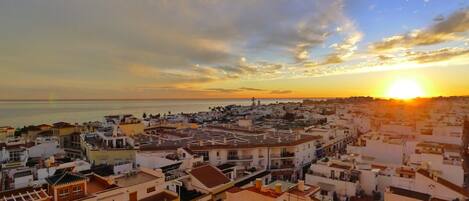 A coastal cityscape at sunset with buildings and a view of the sea.