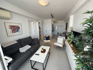 A living room with a sofa, a coffee table, a TV, and a plant.