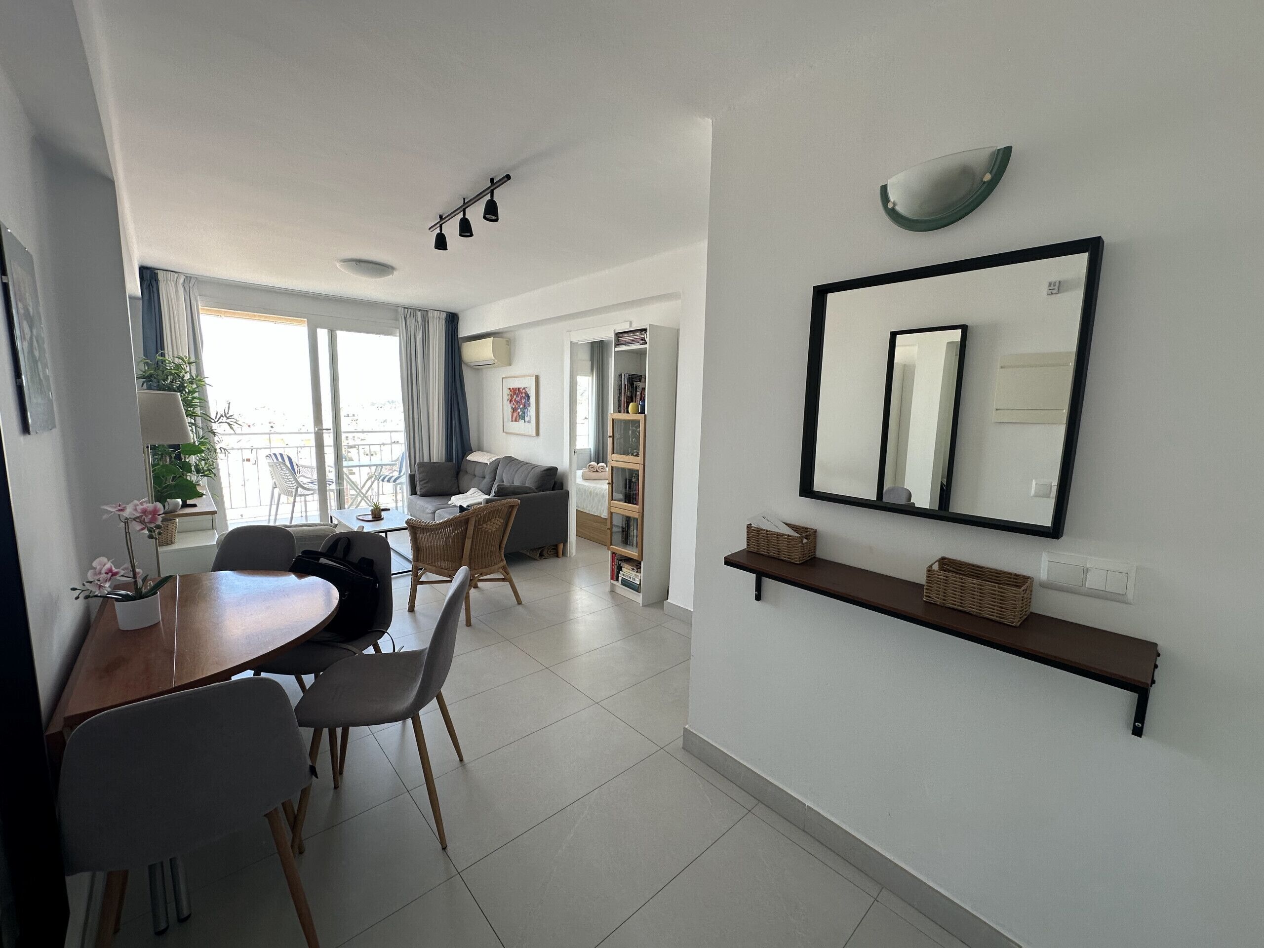 A modern living room with a dining area, a large mirror, and a balcony with plants.