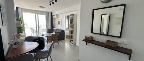 A modern living room with a dining area, a large mirror, and a balcony with plants.