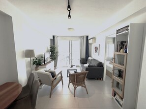 Uma sala de estar com sofá, cadeiras, mesa de centro, estante e janela com cortinas.