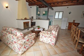A living room with floral sofas, a fireplace, a television, and a kitchen area with a refrigerator and wooden dining table. - Private villa for 4 with a pool, A/C and tennis court (Arezzo)