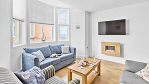 A modern living room with a blue sofa, a grey sofa, a wooden coffee table, and a TV mounted on the wall.
