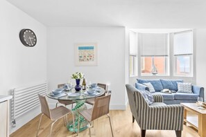 Ein modernes Wohnzimmer mit einem Esstisch mit Glasplatte, einem blauen Sofa und einem gestreiften Sessel.