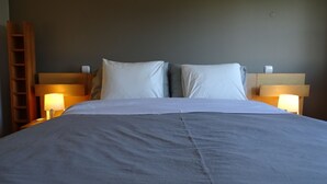 Een opgemaakt bed met een grijze dekbedovertrek, twee witte kussens en twee nachtlampjes aan weerszijden.