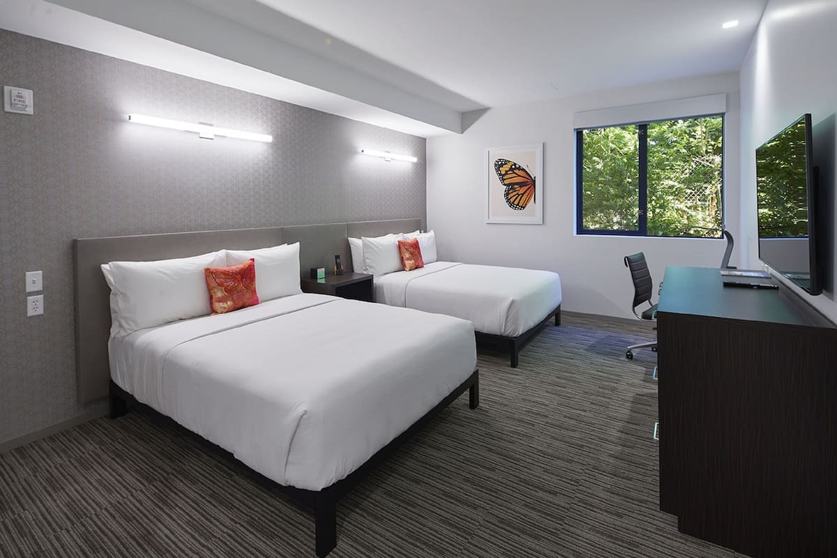 Une chambre d’hôtel avec deux lits, un bureau et une grande fenêtre.