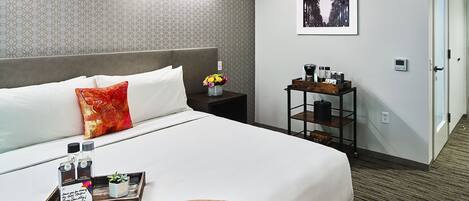 Una habitación de hotel con una cama, una mesita de noche con un jarrón de flores, una bandeja con artículos de aseo y un cuadro en la pared.