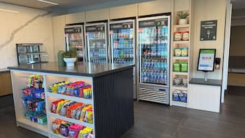 A self-checkout area with a digital payment terminal, a refrigerated beverage dispenser, and a snack display.