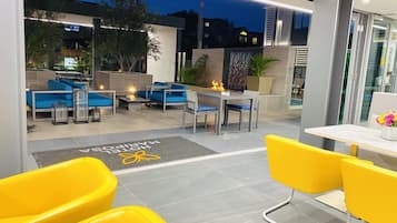 An outdoor seating area with yellow chairs and blue sofas, a fire pit, and a welcome mat with the hotel's name.