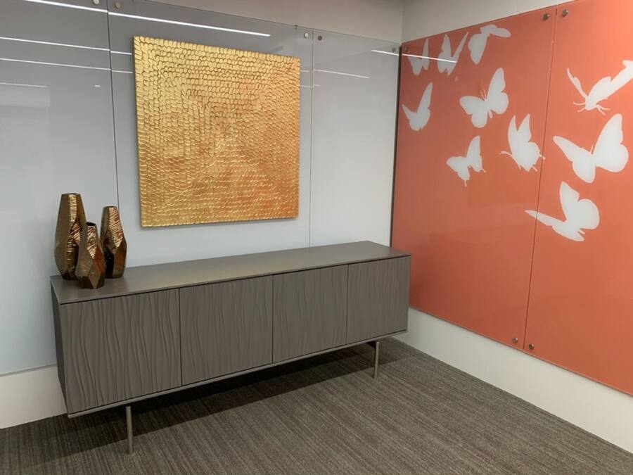 A modern office space with a grey console table, a textured gold artwork, and a wall with white butterfly decals.