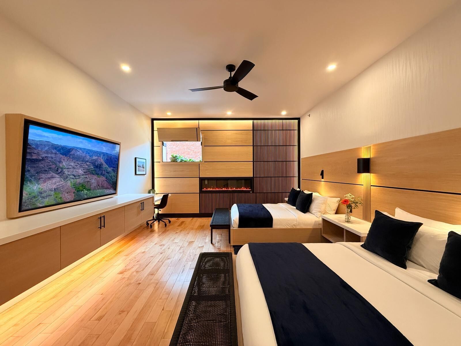 A modern hotel room with a large bed, a desk, a TV, and a fireplace.