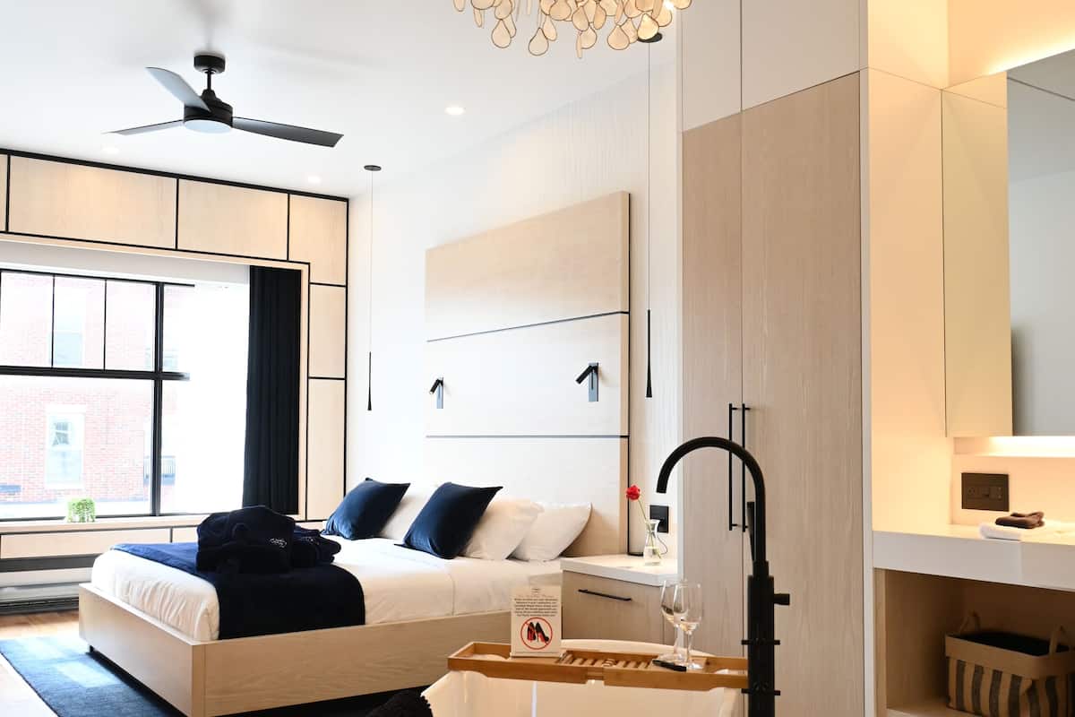 A modern bedroom with a large bed, a unique chandelier, a ceiling fan, and a view of the outside.
