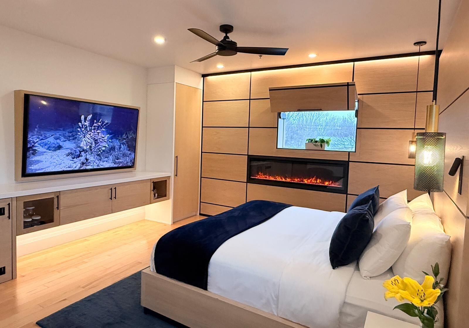 A modern bedroom with a bed, TV, built-in shelves, and a fireplace.