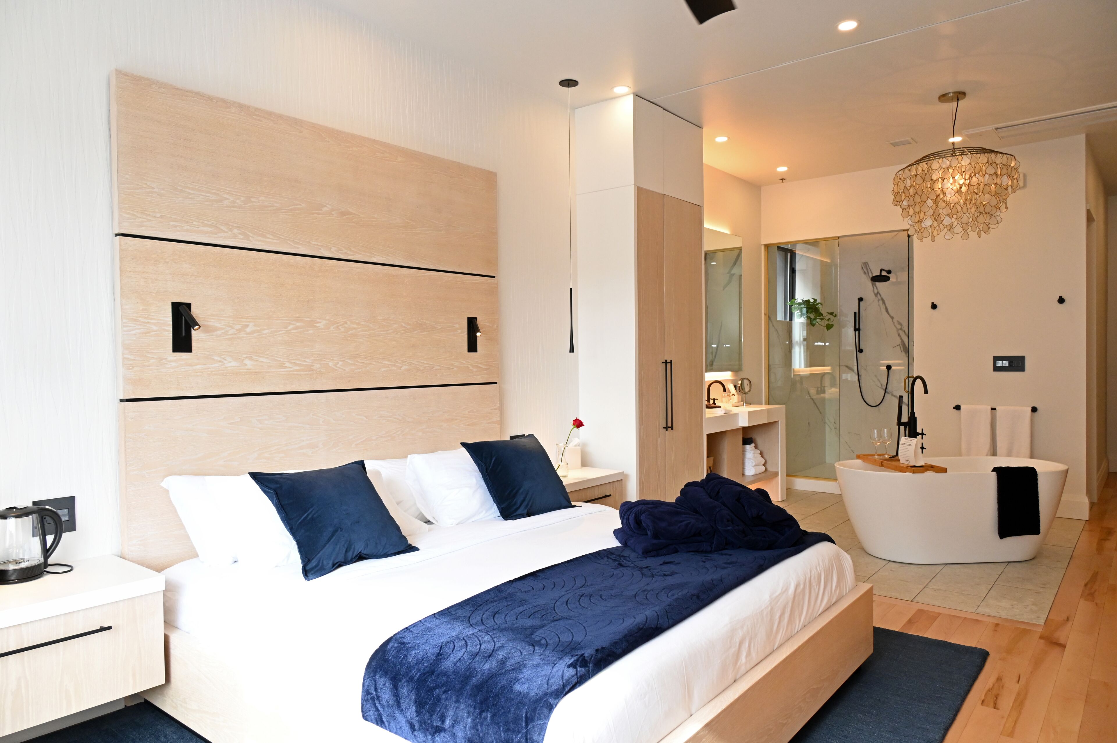 A modern hotel room with a large bed, a separate bathroom with a freestanding bathtub, and a minimalist design.