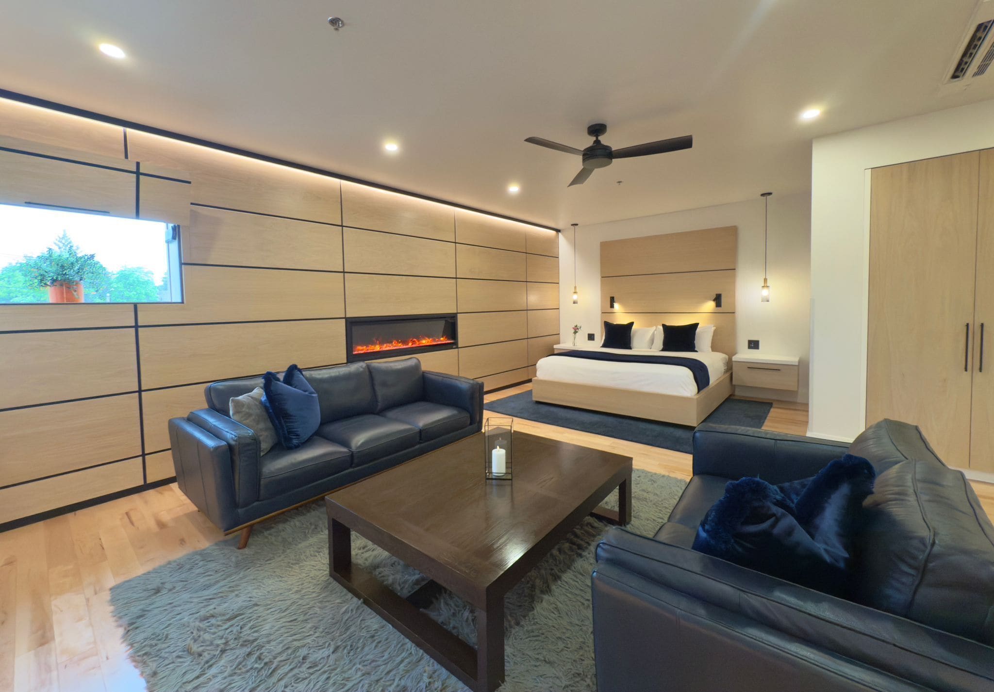 A modern living room with a fireplace, sofas, a coffee table, and a bed with a headboard.