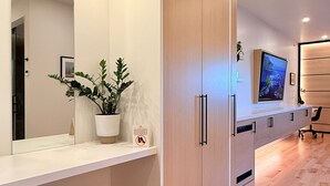 A modern hotel room with a large mirror, wooden wardrobe, a flat-screen TV, and a potted plant. - Cribs on Main (Prince Edward)