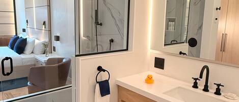 A modern bathroom with a glass shower enclosure, a large mirror, and a wooden vanity with a sink and towel rack.