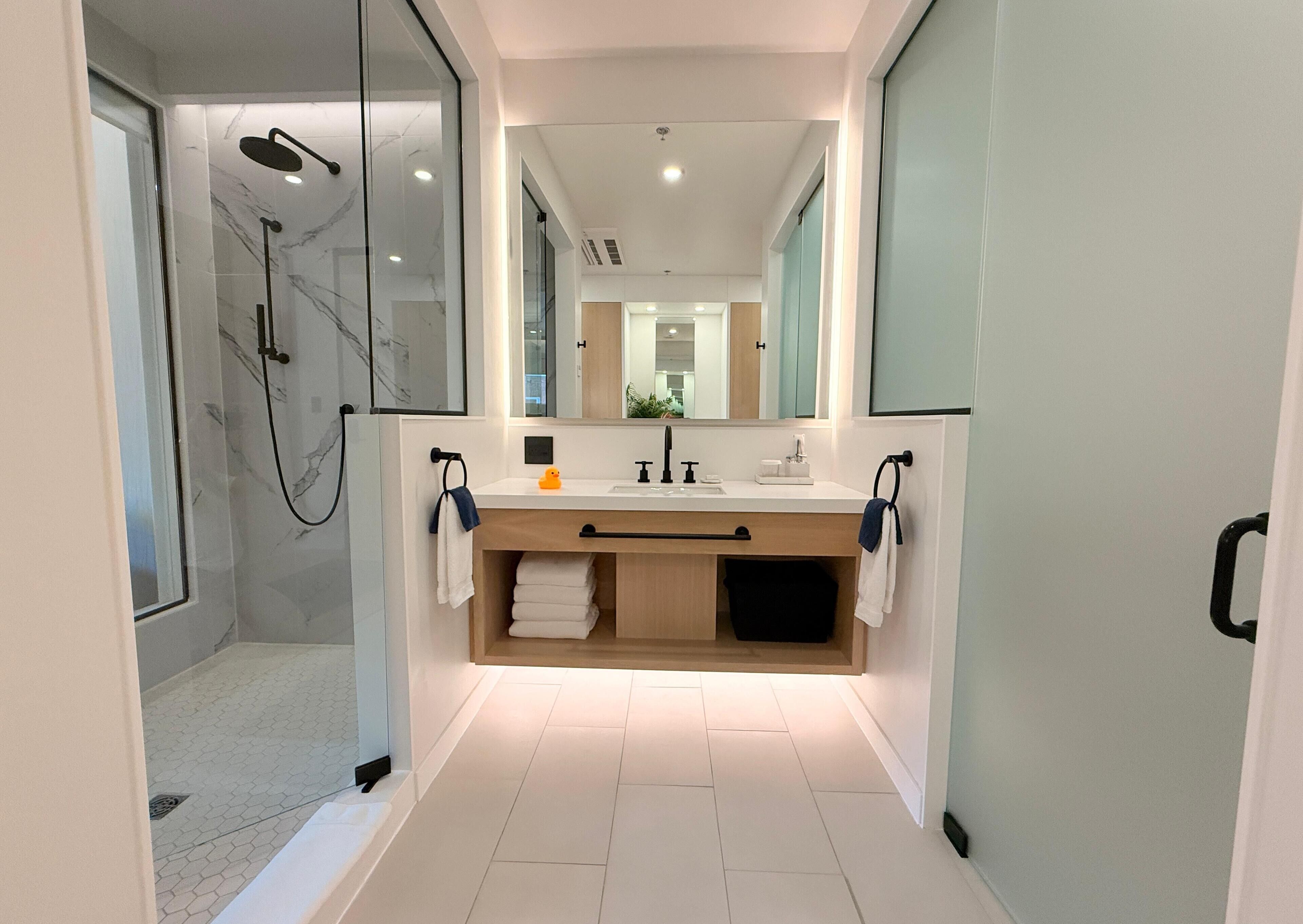 A modern bathroom with a glass-enclosed shower, a vanity with a mirror, and a tiled floor.