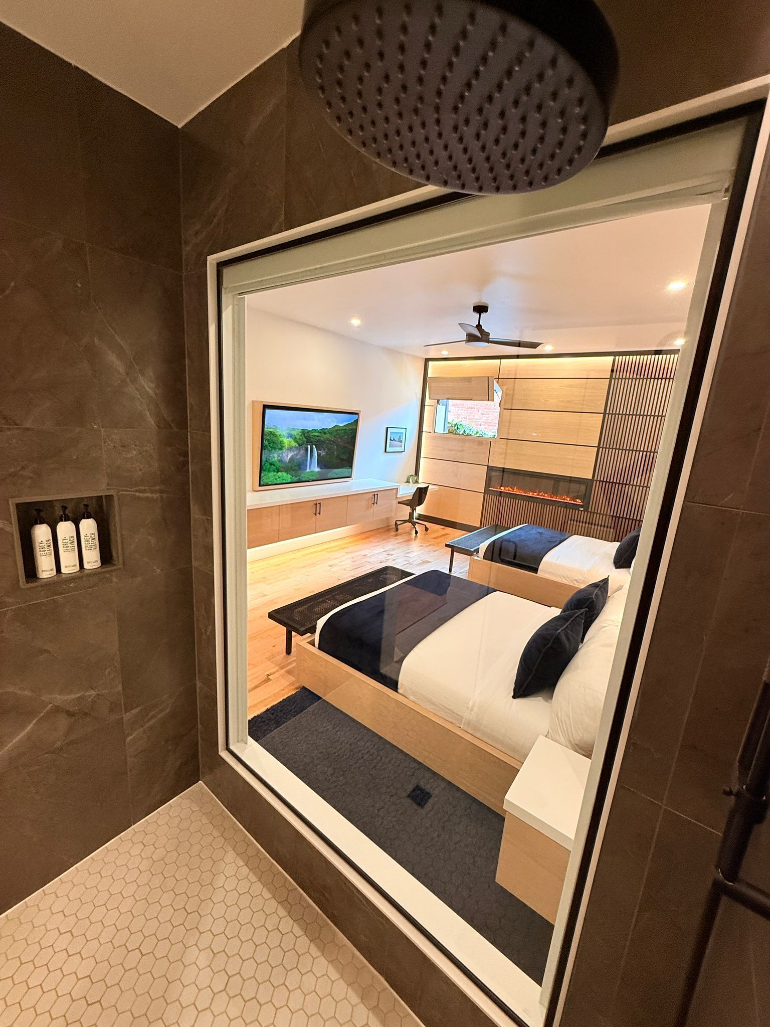 A modern hotel room with a large mirror reflecting a bed, a desk, and a TV.