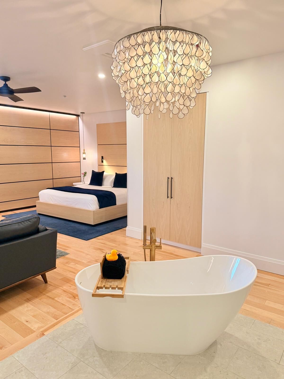 A modern bedroom with a large bathtub, a wooden wardrobe, and a ceiling fan.
