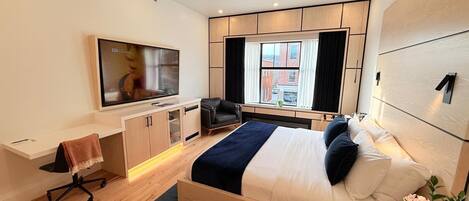 A modern hotel room with a large bed, a desk with a chair, a flat-screen TV, and a ceiling fan.
