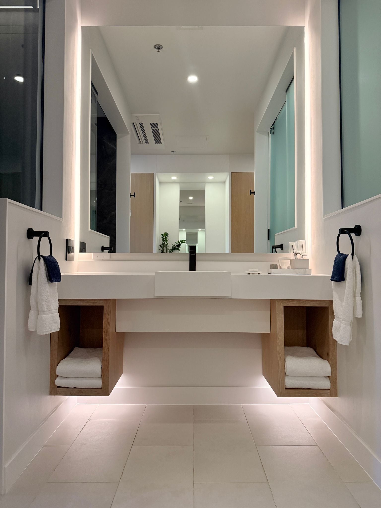 Un baño moderno con un espejo grande, lavamanos dobles y toalleros empotrados.