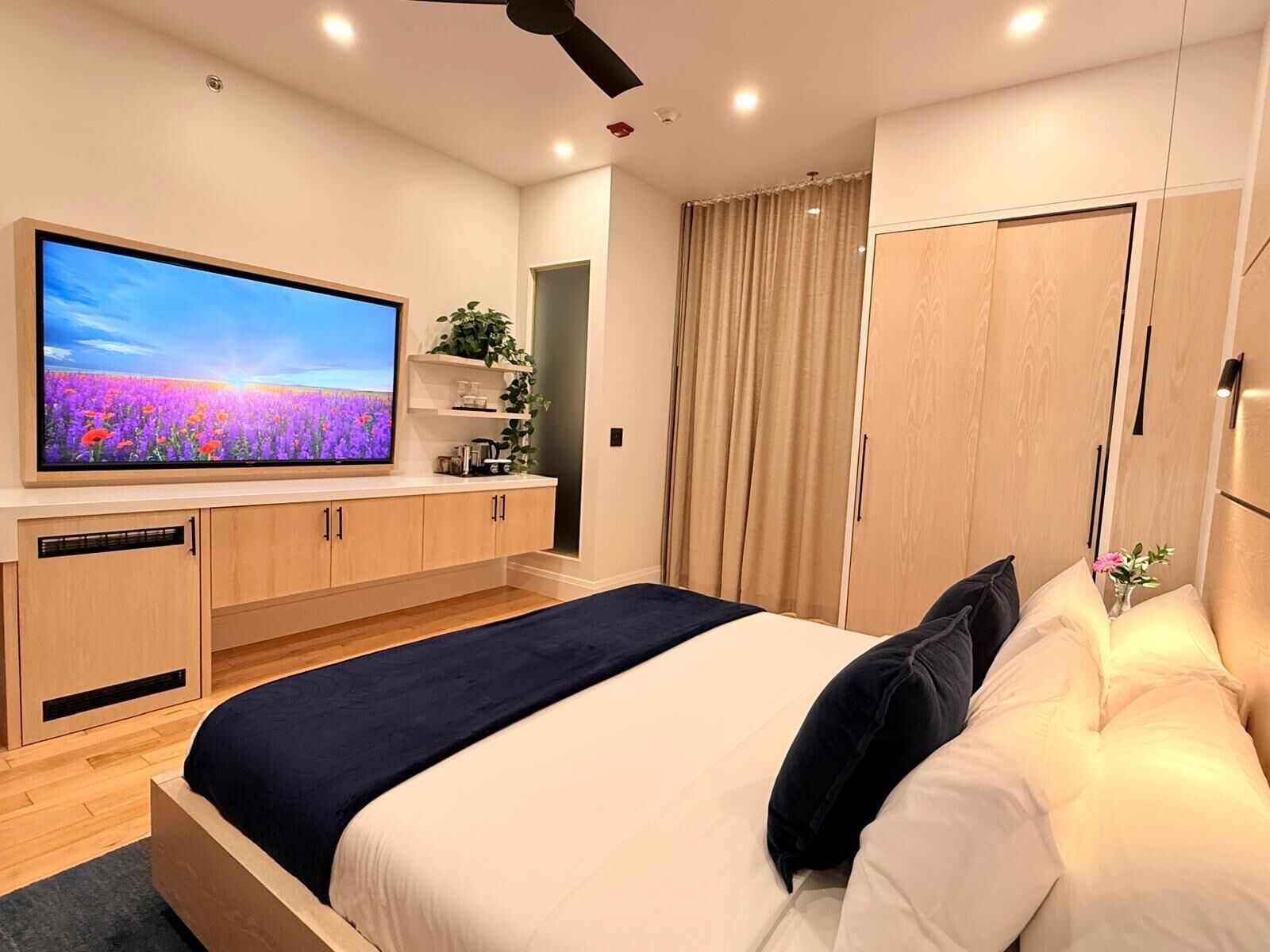 Un dormitorio moderno con una cama grande, un televisor de pantalla plana, armarios de madera, un guardarropa y un ventilador de techo.