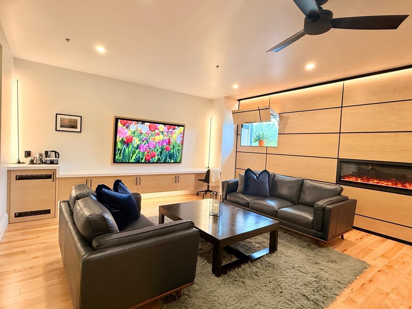 A modern living room with a fireplace, leather sofas, a coffee table, and a flat-screen TV.